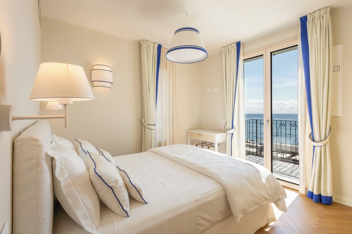 A hotel room with a bed, a desk, and a view of the sea through a sliding door.