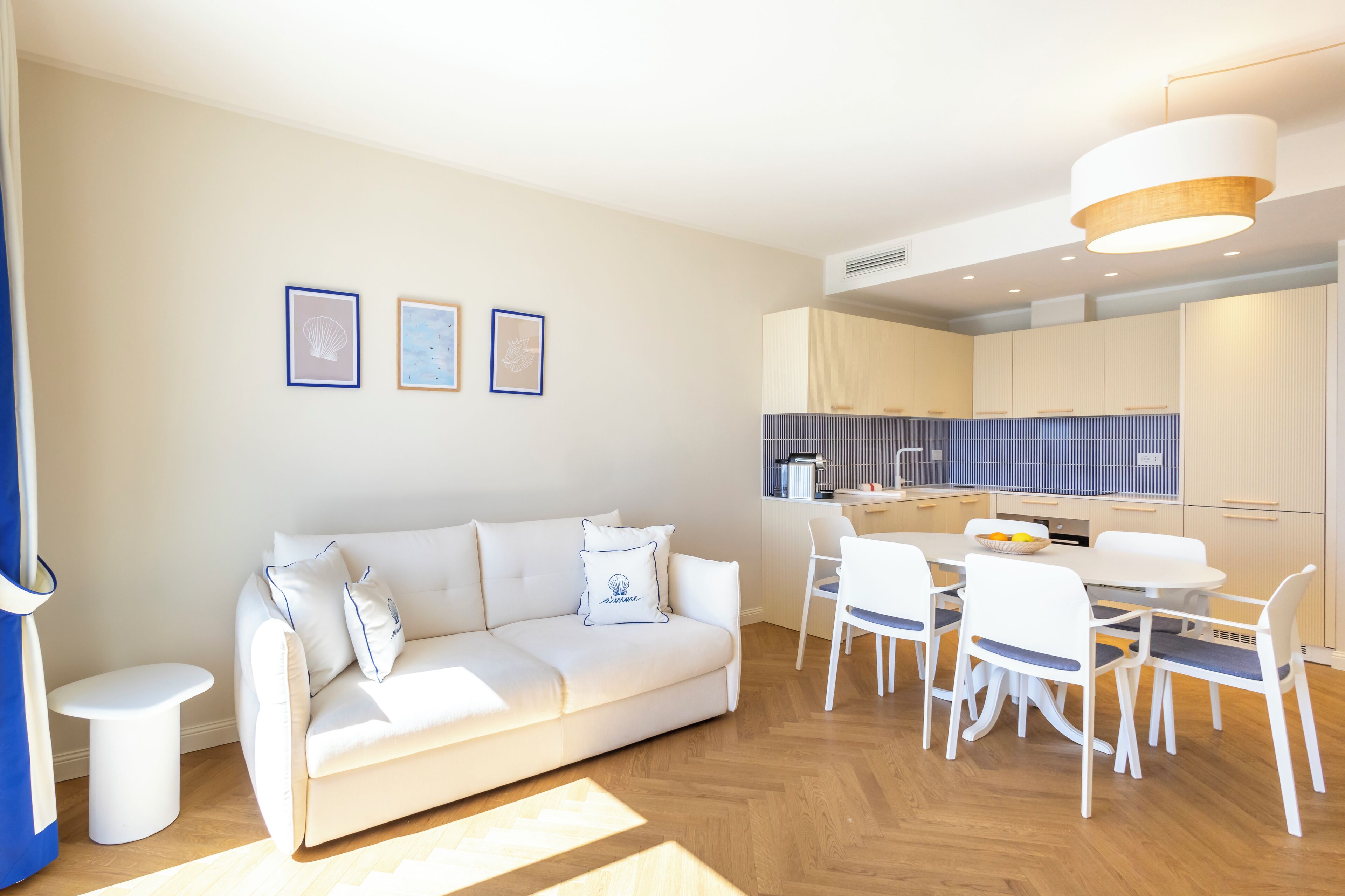 A modern living room with a white sofa, a dining table with chairs, and a kitchen area in the background.