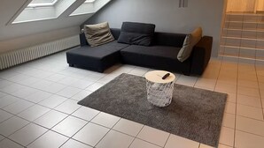 Et moderne loftværelse med en hjørnesofa, ovenlysvinduer, en radiator og en lille plante.