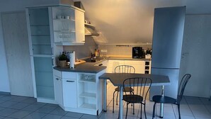 Et lille køkken med spiseplads, hvide skabe og et køleskab.