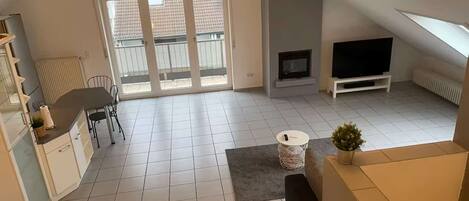 A spacious living area with a sliding glass door leading to a balcony, a flat-screen TV, and a small seating area.