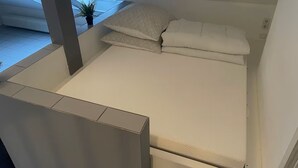 Et kompakt, moderne værelse med seng, ovenlys og en lille potteplante.
