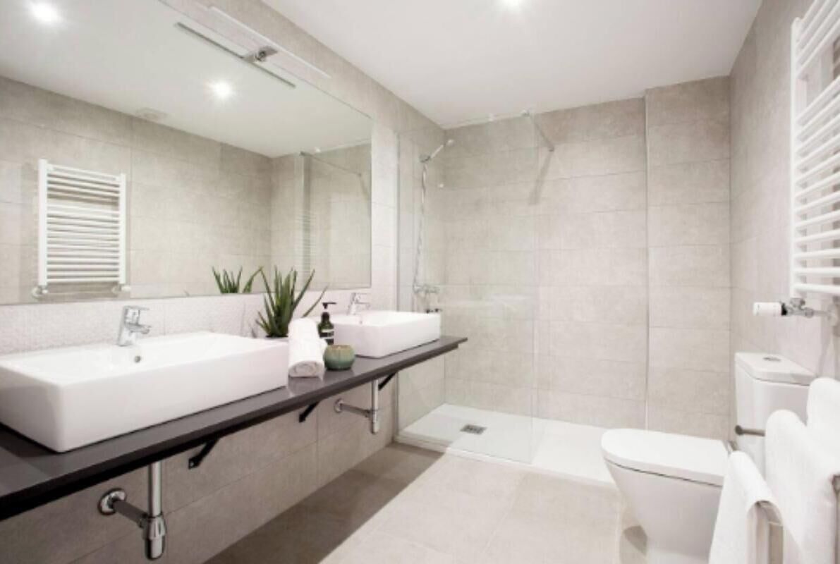 A modern bathroom with a large sink, a mirror, a shower, and a toilet.