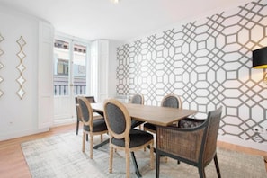 Un comedor con una mesa de madera y cuatro sillas, un papel tapiz estampado y vistas a un balcón.