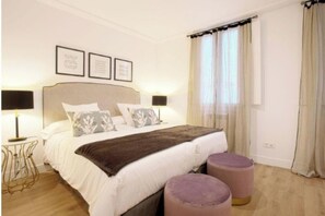 Un dormitorio con cama, mesitas de noche, cabecero y cortinas.