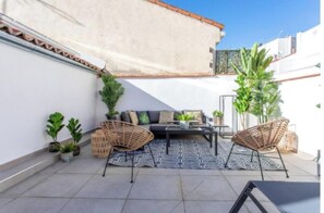 Un patio con un sofá, dos sillones de mimbre, una mesa de centro y plantas en macetas.