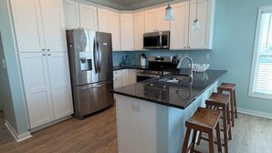 A modern kitchen with white cabinets, stainless steel appliances, a central island with stools, and a pendant light. - A Spacious 4 bedroom 4.5 bath Coastal Escape - Walk to the Beach (Port St. Joe)