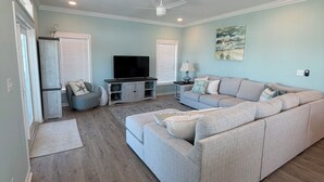 A modern living room with a sectional sofa, a flat-screen TV, and a ceiling fan. - A Spacious 4 bedroom 4.5 bath Coastal Escape - Walk to the Beach (Port St. Joe)