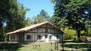 Ein traditionelles Fachwerkhäuschen mit Strohdach, umgeben von einer grünen Wiese und Bäumen.