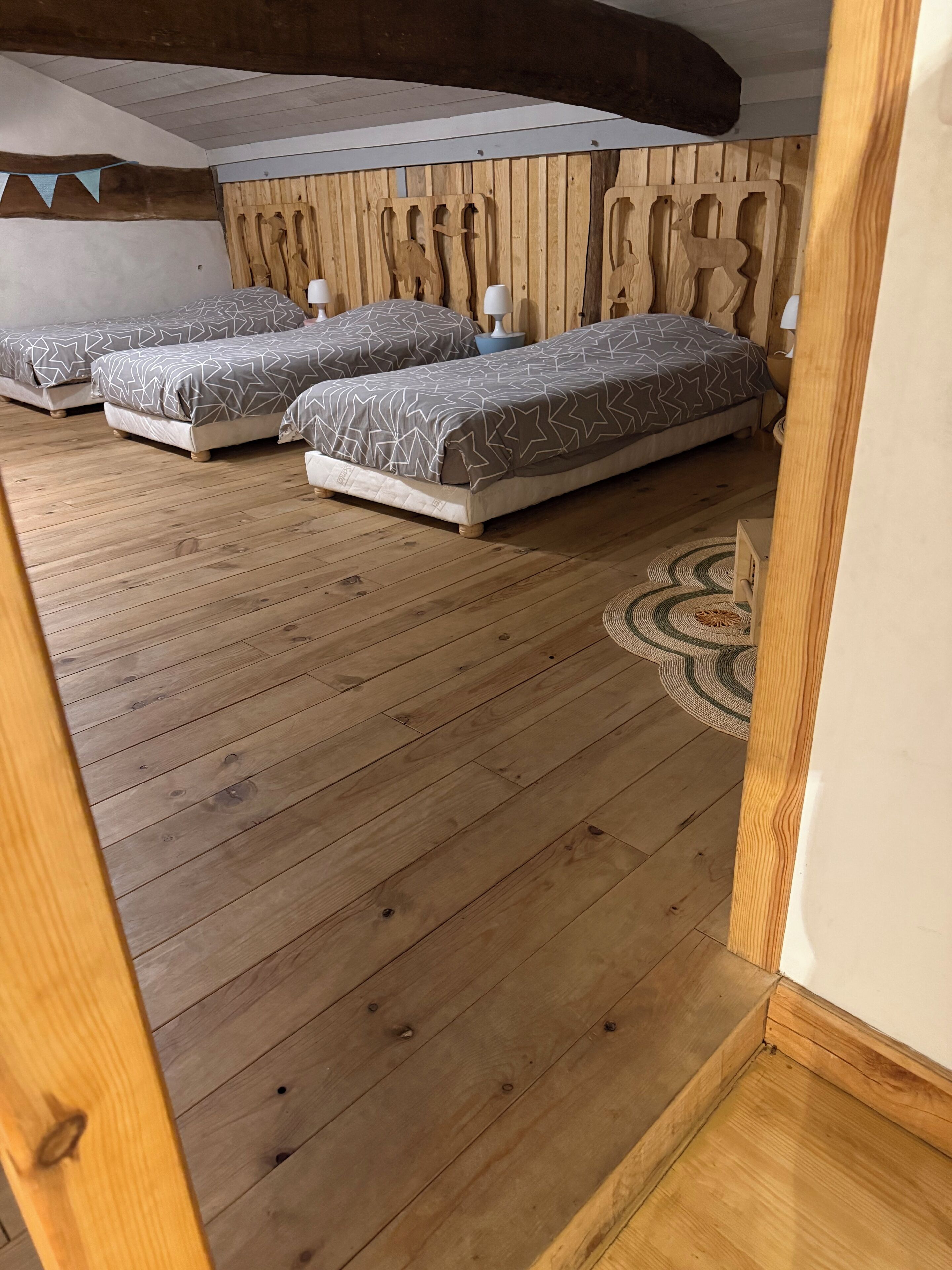 A room with three beds, wooden flooring, and a decorative wall panel.