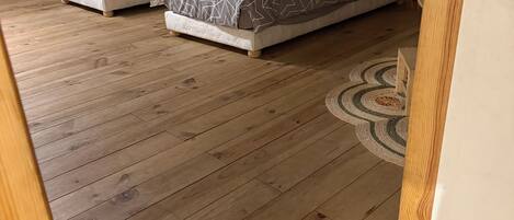 A room with three beds, wooden flooring, and a decorative wall panel.