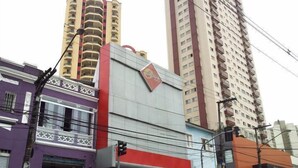 A multi-story building with a prominent red and white sign, surrounded by other buildings. - Option Hotel São Paulo - Anhembi - Expo  (São Paulo)