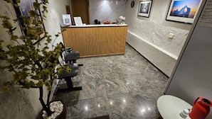 A reception area with a wooden desk, a reception counter, a potted plant, a seating area, and a wall-mounted TV. - Option Hotel São Paulo - Anhembi - Expo  (São Paulo)
