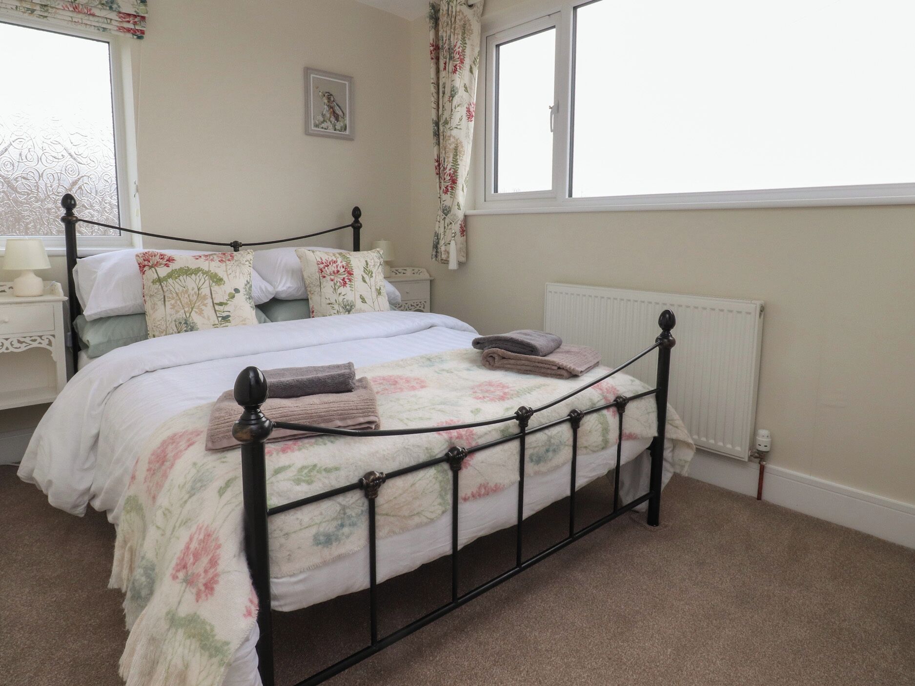 A neatly made bed with floral bedding, a bedside table with a lamp, and a window with floral curtains.