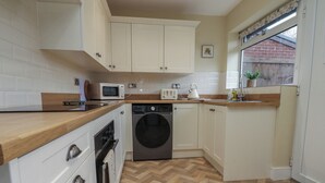 Een kleine keuken met witte kastjes, een magnetron, een broodrooster en een wasmachine.