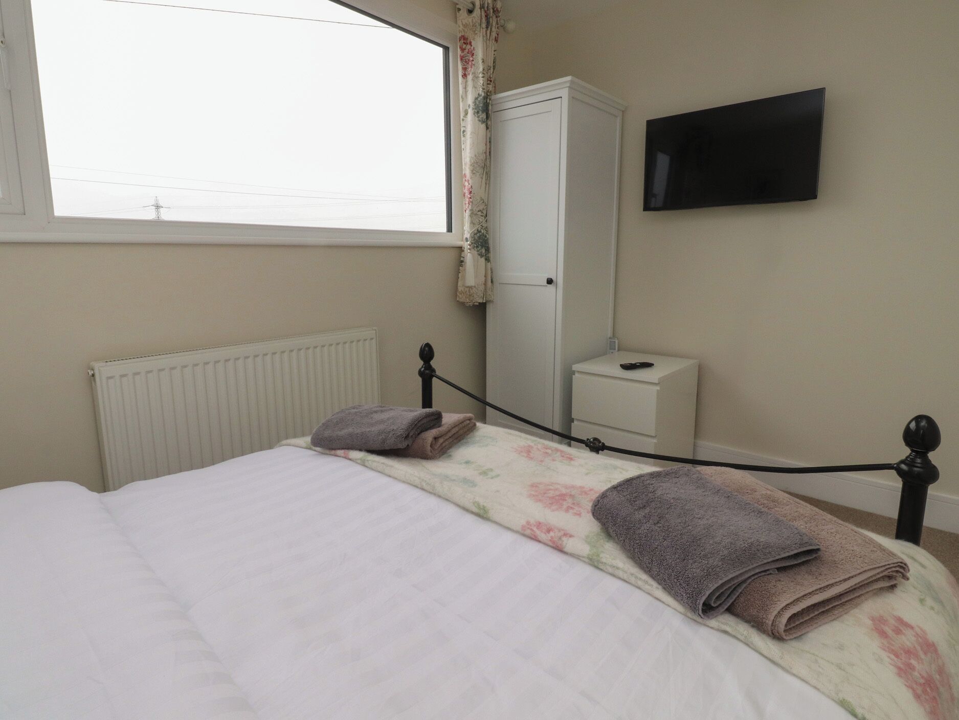 Une chambre à coucher comprenant un lit, un radiateur, une armoire, une table de chevet et un téléviseur fixé au mur.
