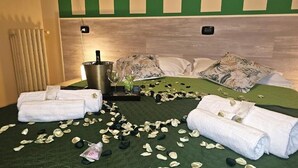 A hotel room with a green bedspread, white pillows, and a metal bucket on the side.