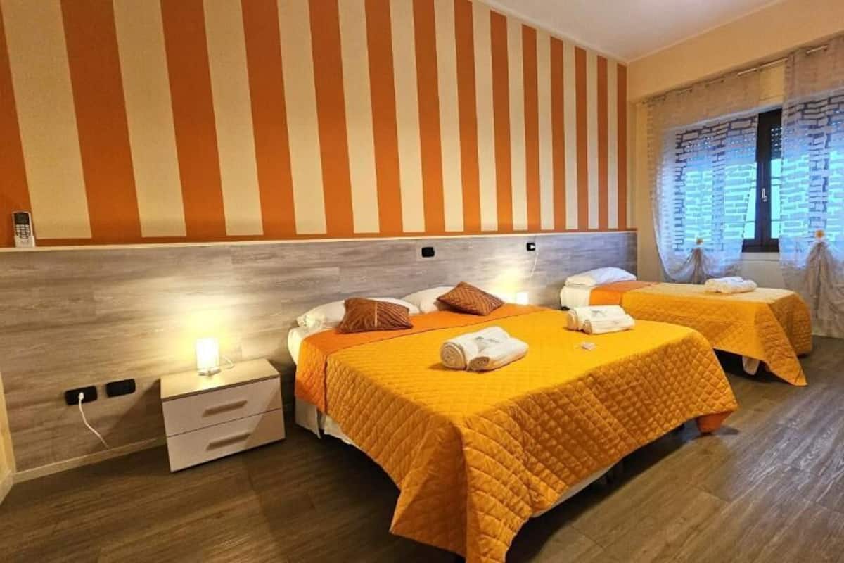 Habitació d'hotel amb dos llits, paper pintat a ratlles, terra de fusta i una finestra amb cortines.