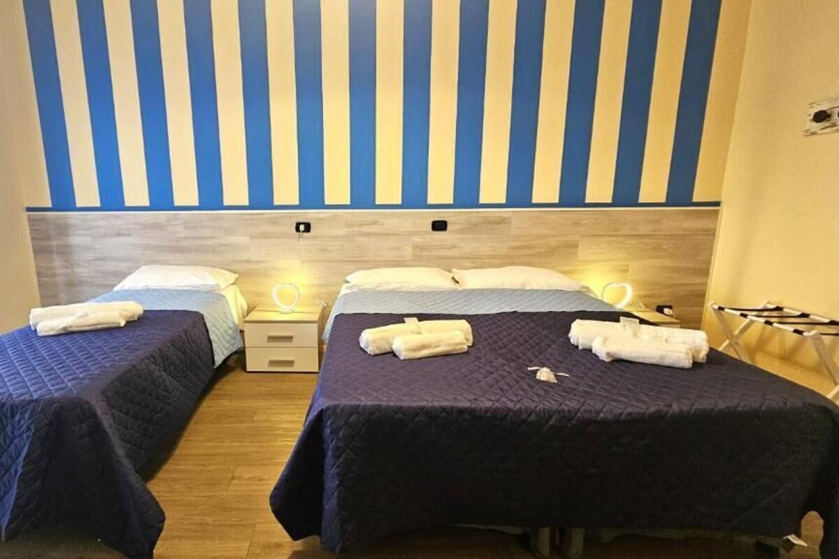 Habitació d'hotel amb dos llits, cadascun amb estovatge blau i almoades blanques. Hi ha taules de nit amb làmpades i tovalloles plegades sobre cada llit.