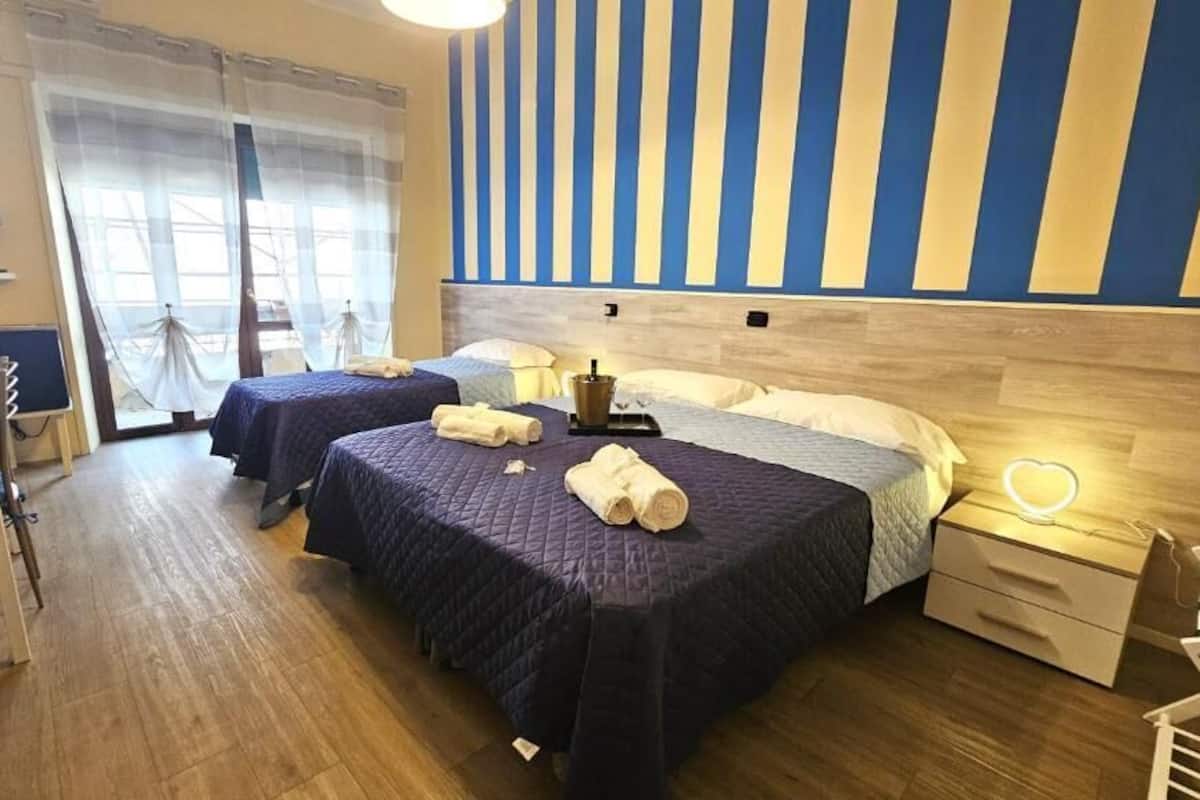 Una habitació d'hotel amb dos llits, un sòl de fusta, una paret amb ratlles i una taula de nit amb una làmpada.