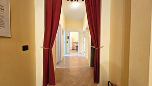 A hallway with red curtains, beige walls, and a tiled floor leading to a room.