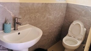 Een badkamer met een wastafel, toilet en een kleine afvalbak.