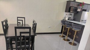 Een keuken met een eettafel en stoelen, een bar met krukken, en een magnetron boven het aanrecht.