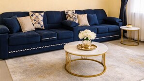 Een woonkamer met een donkerblauwe bank, een ronden bijzettafeltje met gouden lijst en een witte marmeren tafel.