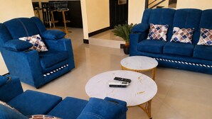 Una habitación con sofás azules, una mesa de centro blanca y una silla negra.