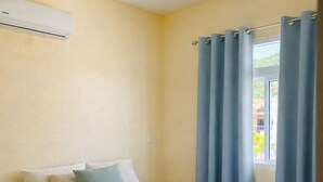 Een slaapkamer met een bed, een raam met gordijnen en een airconditioning aan de muur.