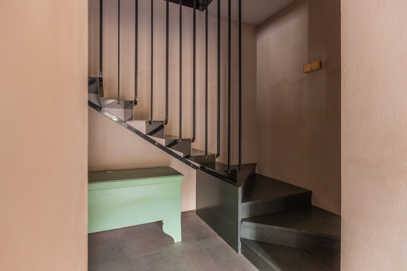 A staircase with a green bench at the bottom, a light switch on the wall, and a door frame.