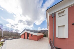 A modern building with a red facade and a flat roof, adjacent to a paved area with a metal railing. - La Casa di Caterina - Camera 3 (Atripalda)