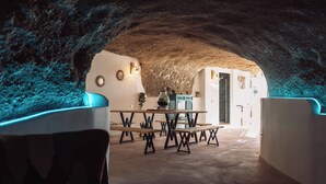 Un interior con techo de piedra rústica, una zona de comedor con bancos y mesas de madera, y una cocina visible a través de un arco.