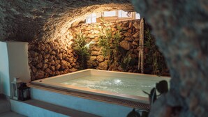 Tinaja de piedra con agua, rodeada de plantas, y un farol en un repisa.