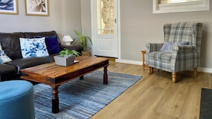 A living room with a dark leather sofa, a wooden coffee table, a plaid armchair, and a large mirror on the wall. - Bronafon (Rhyl)