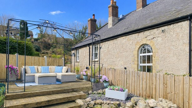 A stone house with a wooden deck, outdoor seating, and a stone wall. - Bronafon (Rhyl)