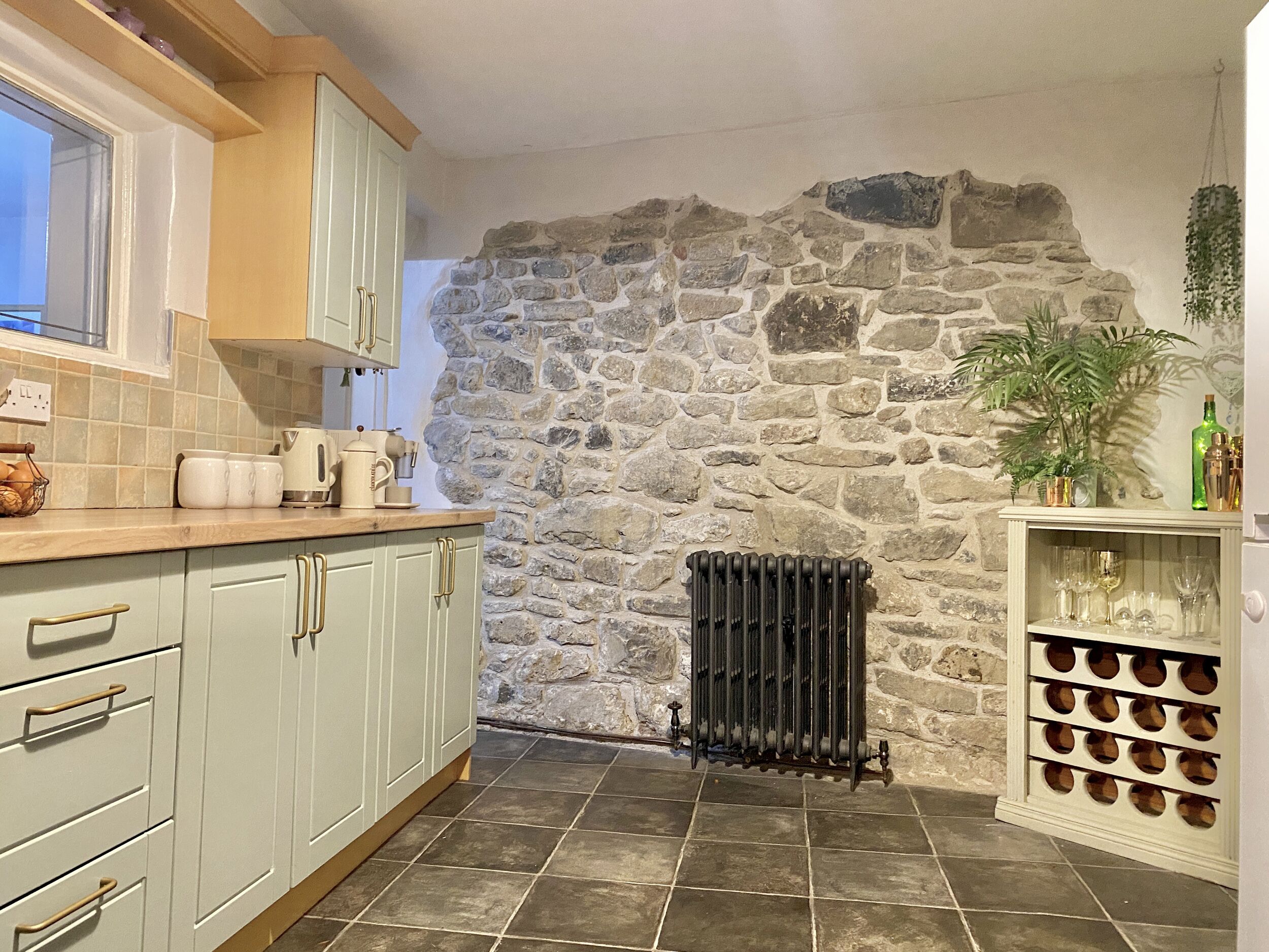 A kitchen with light green cabinets, a stone wall, a radiator, and a wine rack.