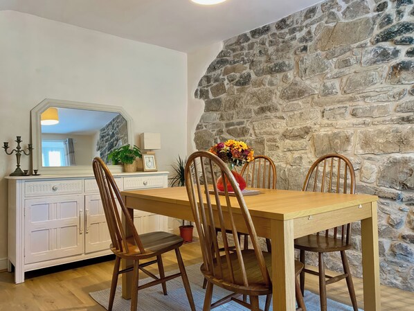 A dining area with a stone wall, wooden table, and chairs. - Bronafon (Rhyl)