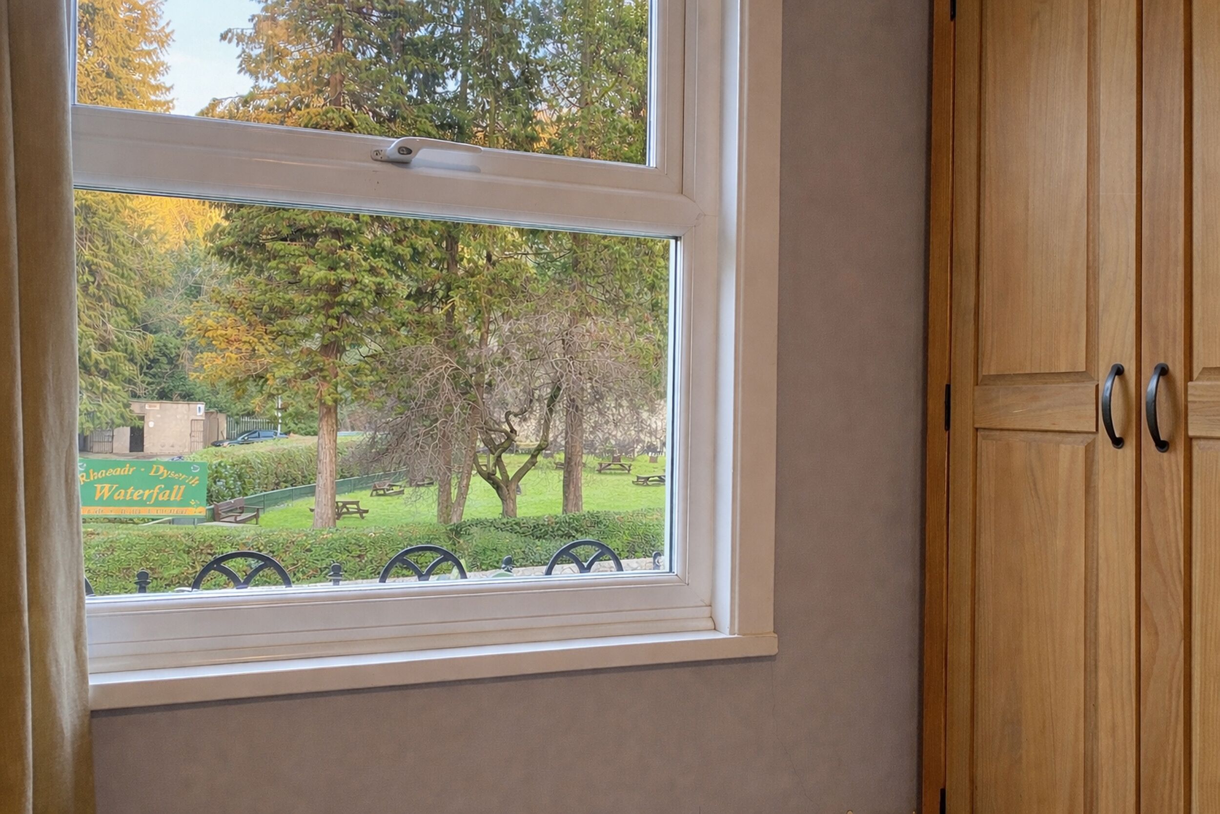 A room with a window offering a view of a park and a sign for a waterfall.