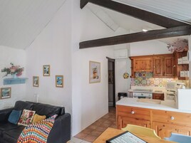 Una sala de estar con un sofá de cuero negro, una mesa de comedor de madera y una cocina con armarios de madera y salpicadero de azulejos.