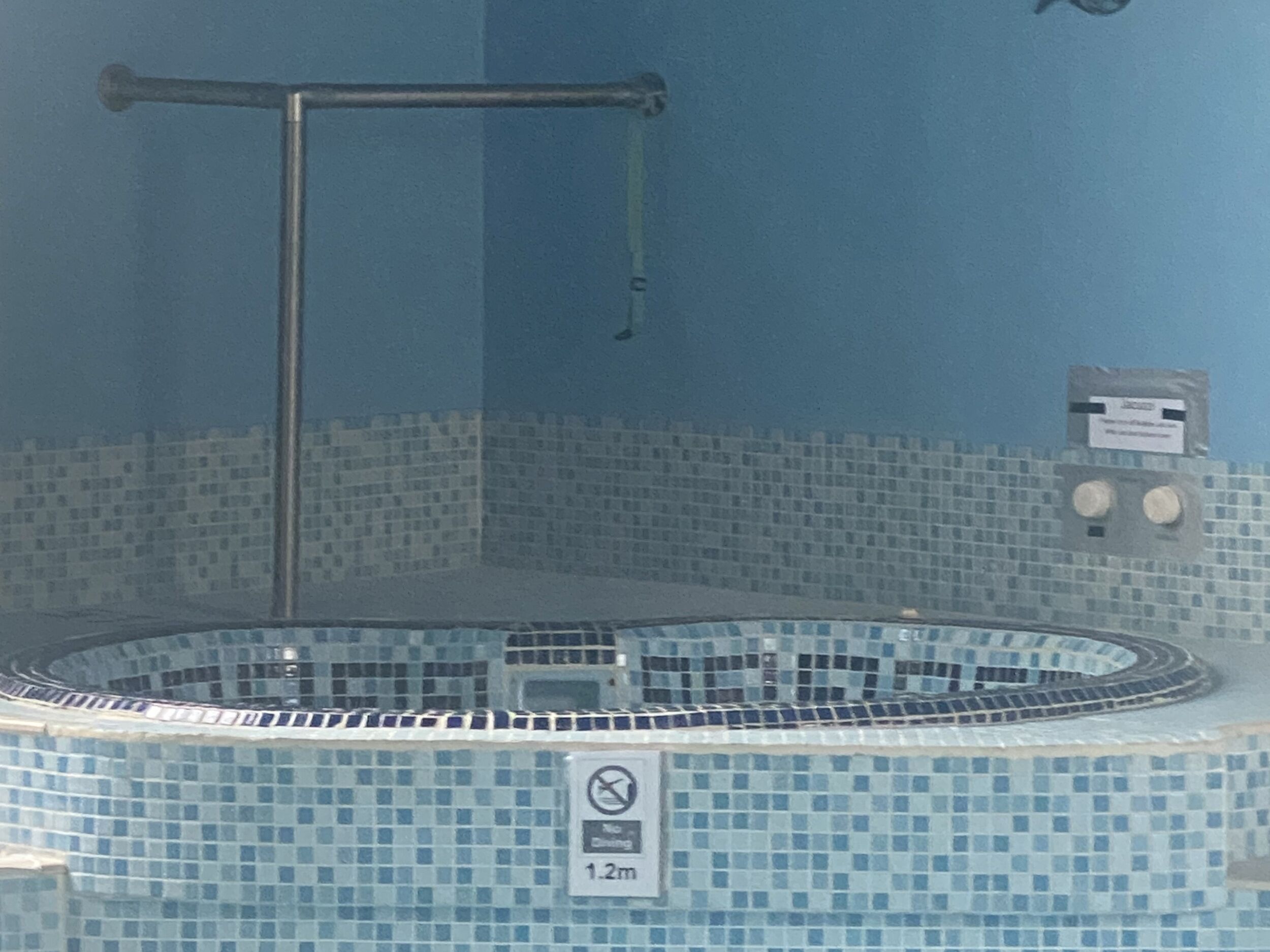 Uma banheira de hidromassagem com parede azulejada e aviso de proibição de mergulho.