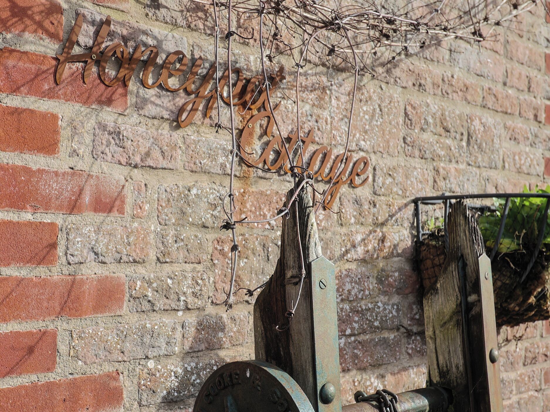 A rustic metal sign with the words "Honeycomb Cottage" against a brick wall.