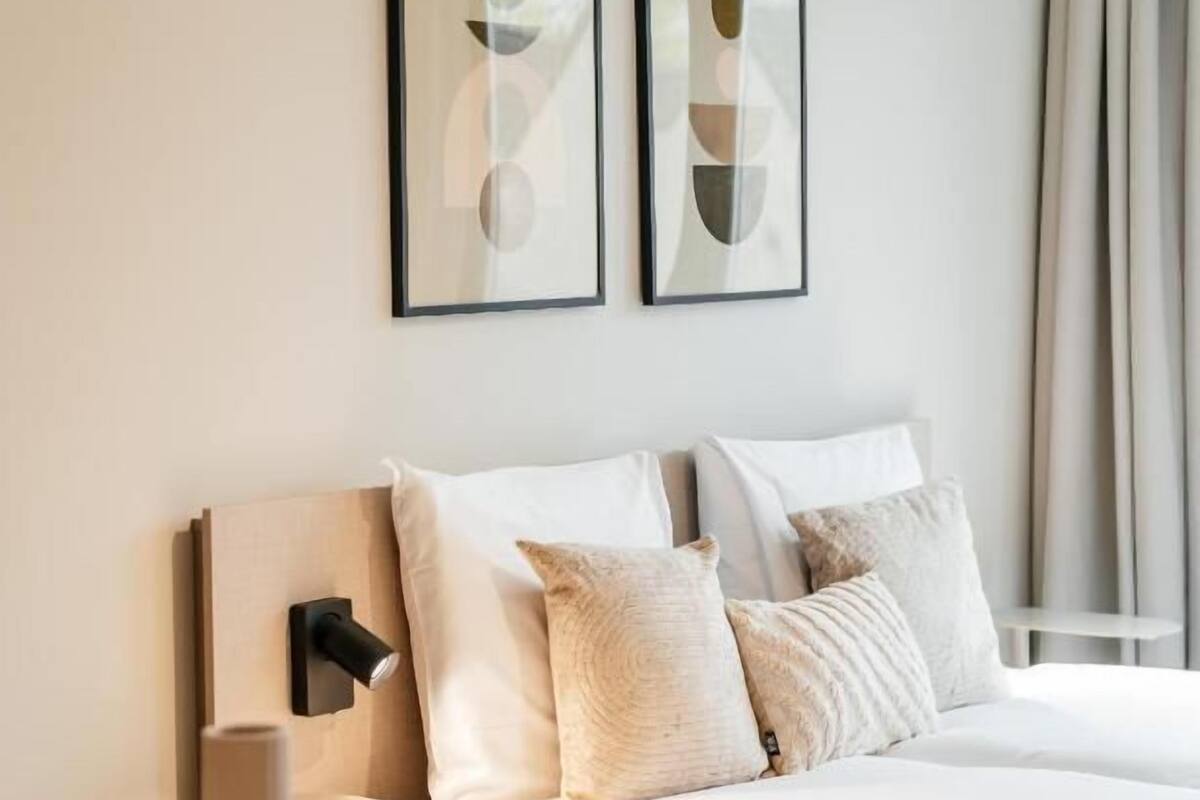 Ein ordentlich eingerichtetes Hotelzimmer mit einem Bett, einem Nachttisch mit einer Vase und zwei gerahmten abstrakten Kunstwerken an der Wand.