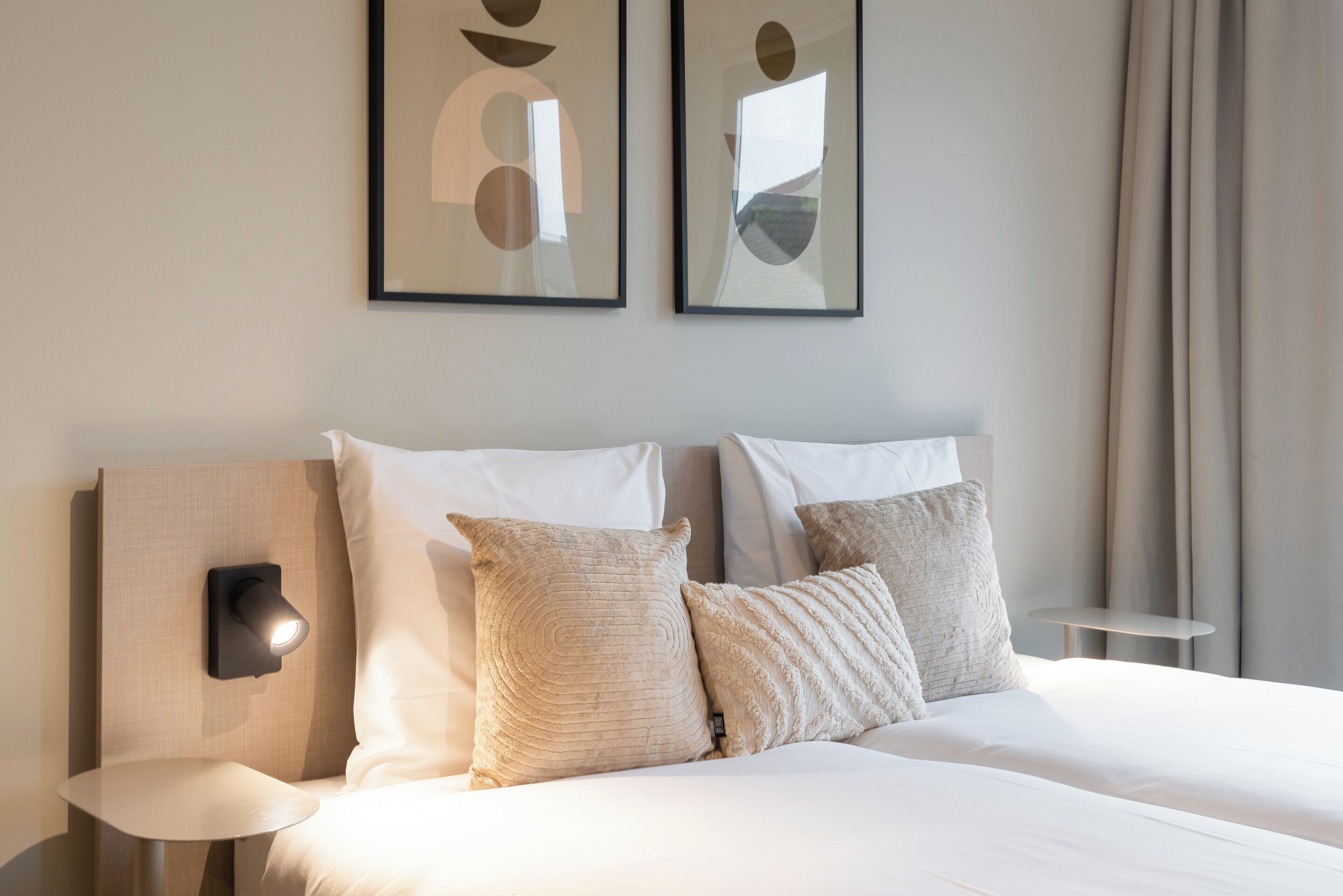 Une chambre d’hôtel comprenant un lit, deux oreillers, une table de chevet, une lampe et deux œuvres d’art abstraites accrochées au mur.