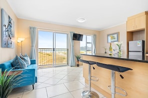 A modern kitchen with a bar area, a blue sofa, and a large window with a view. - Sunrise Villas 91 (Cape Town)