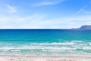 Una playa con aguas turquesas cristalinas y una cadena montañosa a lo lejos.
