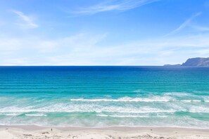 Una spiaggia con acque turchesi cristalline e una catena montuosa all'orizzonte.