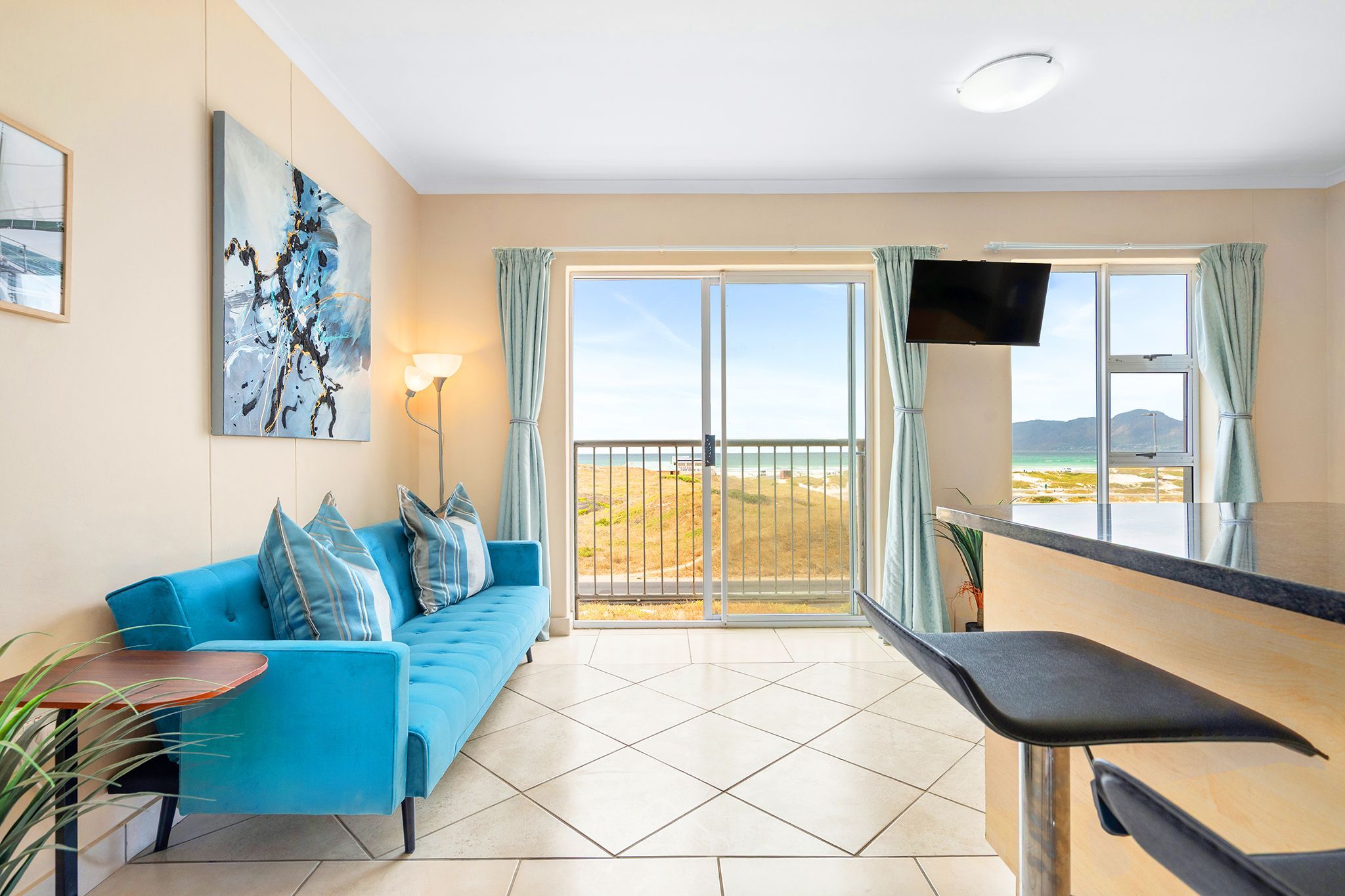 Une chambre moderne avec un canapé bleu, un téléviseur à écran plat et un balcon offrant une vue sur la plage.