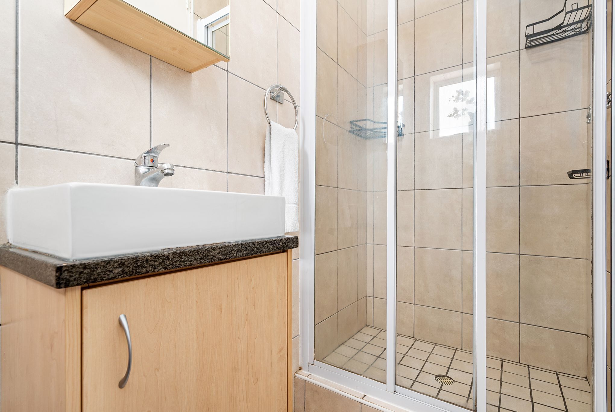 A bathroom with a sink, mirror, and shower area.