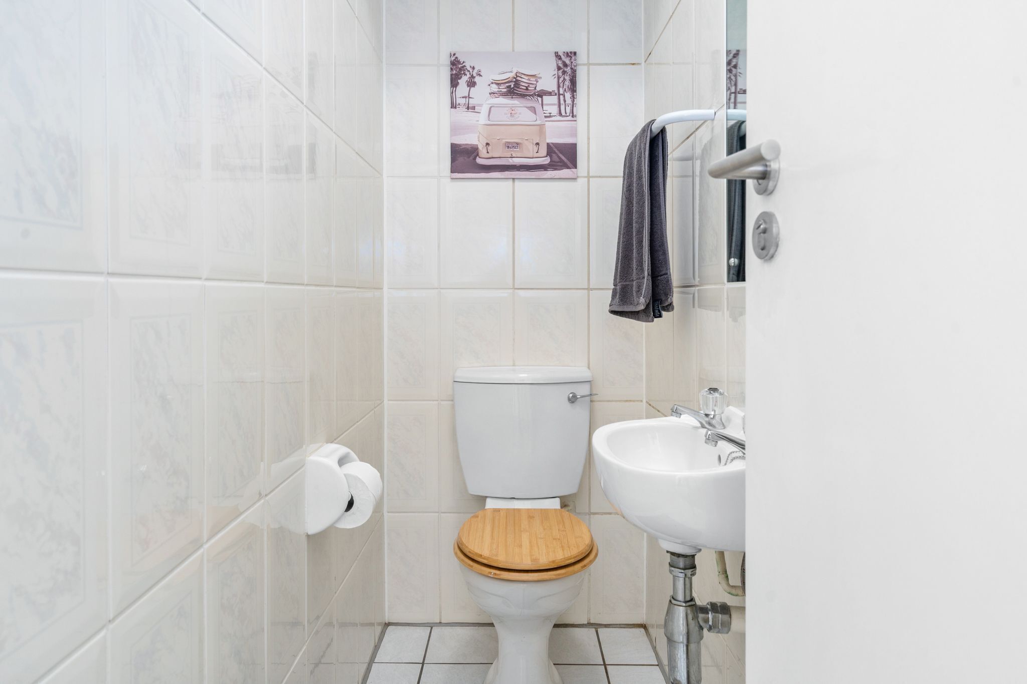 A small bathroom with a toilet, sink, and a picture of a car on the wall.